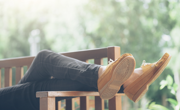Person laying on their back on a bench in the sun with their feet in the air showing the soles of their feet.
